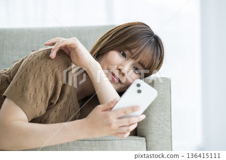 A young woman lying on a sofa and using a smartphone A young woman lying on a sofa and using a smartphone 136415111