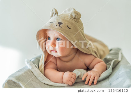 Baby lying on a changing table wrapped in a soft towel after bathing at home. Clean, calm and cozy moment of infant care and safety. Baby hygiene, daily routine and gentle parenting concept 136416120