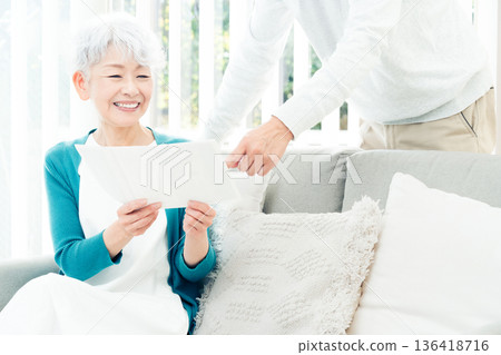 Senior woman looking at documents on the sofa Senior woman looking at documents on the sofa 136418716