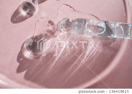 Clear liquid serum with bubbles falling from dropper creating reflections on pink surface 136419615