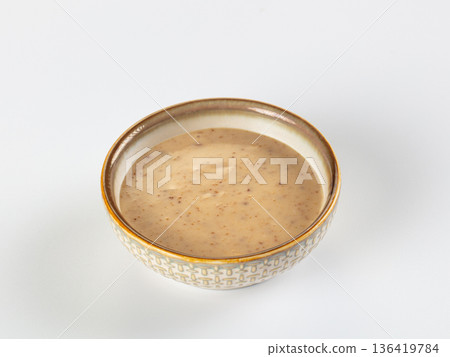 Creamy nut or seed sauce in a decorative ceramic bowl, isolated on a white background. Creamy nut or seed sauce in a decorative ceramic bowl, isolated on a white background. 136419784