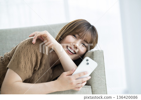 A young woman lying on a sofa and operating a smartphone 136420086