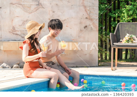 一對年輕夫婦穿著泳裝,在熱帶度假村的泳池畔放鬆身心,這對夫婦正在出國旅行、度蜜月或度假。 一對年輕夫婦穿著泳裝,在熱帶度假村的泳池畔放鬆身心,這對夫婦正在出國旅行、度蜜月或度假。 136420393