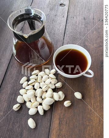 Pistachio nuts and a glass of hot coffee on wooden table Pistachio nuts and a glass of hot coffee on wooden table 136420775