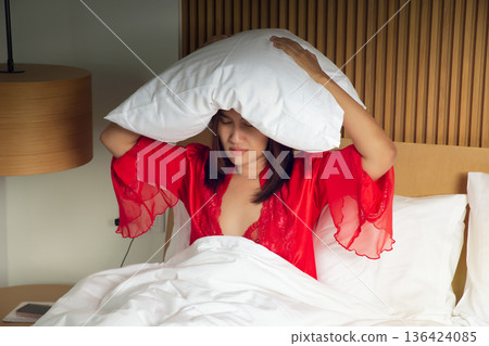 Woman Wearing Red Satin Sleepwear Covering Head With Pillow Due to Insomnia 136424085