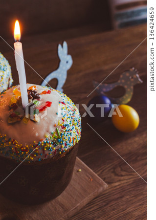 Easter cake with candles and festive decor. Easter still life. Orthodox Eater celebration. Colourful Easter eggs with sweet glazing cakes and lit candles. Spring religious holiday. Christian tradition 136424659