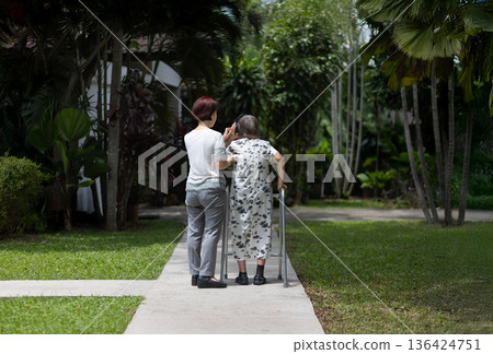 Elderly woman exercise walking in backyard with daughter. Elderly woman exercise walking in backyard with daughter. 136424751