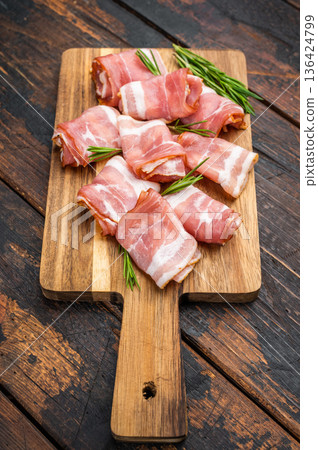 Rolled raw bacon pork rashers on rustic wooden board with rosemary and pepper ideal for cooking recipes and food styling content Rolled raw bacon pork rashers on rustic wooden board with rosemary and pepper ideal for cooking recipes and food styling content 136424799