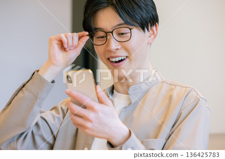 一位戴眼鏡的男子在咖啡館使用智慧型手機。 136425783