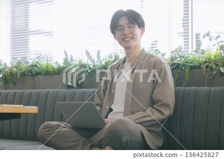 一個男人坐在沙發上使用電腦 136425827