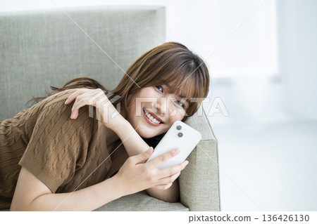 Young woman, smartphone, smiling, looking at camera, sofa 136426130