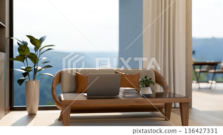 Laptop and books on glass top table and a wooden sofa chair aside window wall with mountain scenery. Laptop and books on glass top table and a wooden sofa chair aside window wall with mountain scenery. 136427331