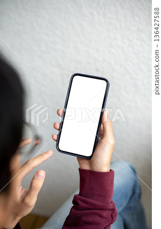 A man holding white screen smartphone looking or reading while sitting beside white wall in a cafe. A man holding white screen smartphone looking or reading while sitting beside white wall in a cafe. 136427588