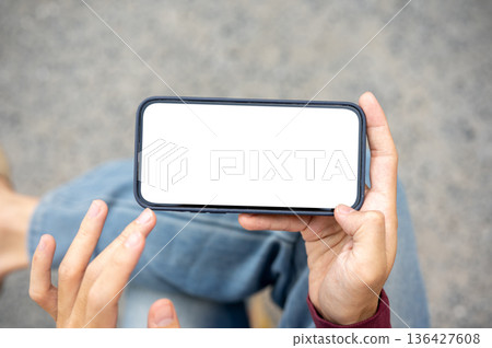 A man hand holding and touching blank screen smartphone in horizontal watching video or playing game A man hand holding and touching blank screen smartphone in horizontal watching video or playing game 136427608