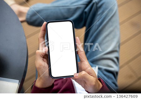 A man holding white screen smartphone with both hands while sitting at table in cafe or coffee shop. A man holding white screen smartphone with both hands while sitting at table in cafe or coffee shop. 136427609