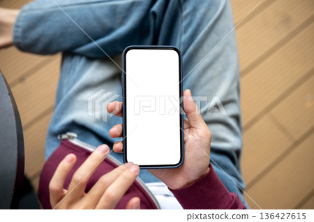 A man holding and touching on blank screen smartphone while sitting at table in cafe or coffee shop. A man holding and touching on blank screen smartphone while sitting at table in cafe or coffee shop. 136427615