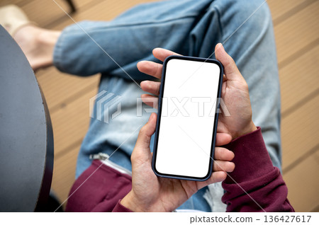 A man's hands holding white screen smartphone while sitting at table in the cafe or coffee shop. 136427617