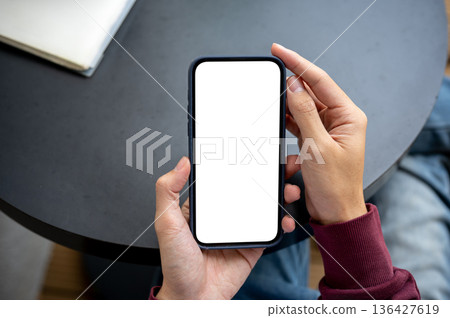 A man hand holding blank screen smartphone reading or looking while sitting at black table in a cafe A man hand holding blank screen smartphone reading or looking while sitting at black table in a cafe 136427619