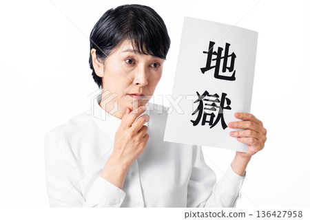 A senior woman with a gloomy expression holding a piece of paper with the word "Hell" written on it A senior woman with a gloomy expression holding a piece of paper with the word "Hell" written on it 136427958