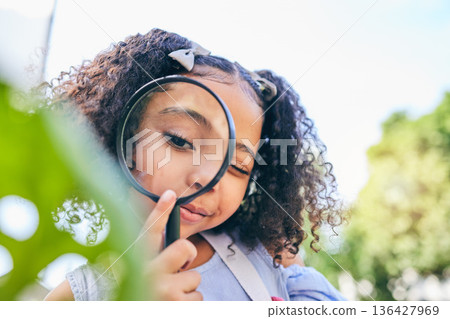 Girl child, magnifying glass and leaves in garden, backyard or park in science, study or outdoor. Young female kid, lens and zoom for nature, research or check for plant, ecology or growth in summer 136427969