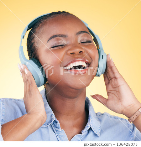 Singing, music and black woman on headphones, smile and listening in studio isolated on a yellow background. Happy, radio and African person streaming podcast, audio and sound, hearing and freedom. 136428073