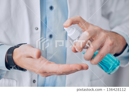 Closeup, hands and doctor, with sanitizer, man and protection from bacteria, disease and virus. Spray, person or medical professional for hygiene, wellness and healthcare with safety and disinfectant 136428112