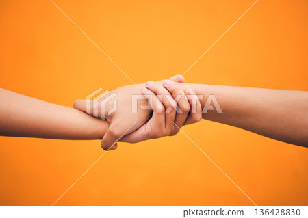 Holding hands, studio and closeup for support, help and care for teamwork by orange background. People, friends and together for solidarity, link and connection with synergy, partnership and strong 136428830
