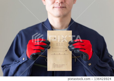 一位身著工作服的中年男性商務人士，手裡拿著薪資袋。 136428924