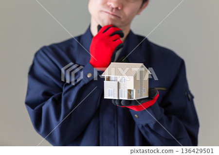 A middle-aged male businessman in work clothes worried about a house model 136429501