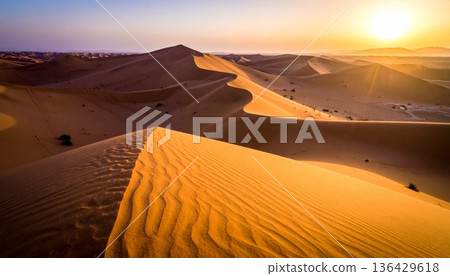 An orange sun sets over the red sand dunes of the Sahara, creating a hot wilderness landscape during a dry summer adventure in the arid Morocco desert An orange sun sets over the red sand dunes of the Sahara, creating a hot wilderness landscape during a dry summer adventure in the arid Morocco desert 136429618