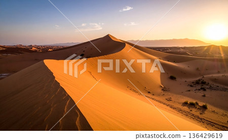 An orange sun sets over the red sand dunes of the Sahara, creating a hot wilderness landscape during a dry summer adventure in the arid Morocco desert 136429619