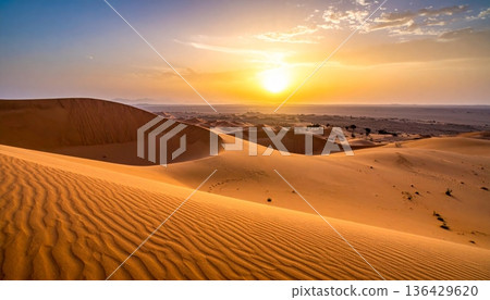 An orange sun sets over the red sand dunes of the Sahara, creating a hot wilderness landscape during a dry summer adventure in the arid Morocco desert 136429620