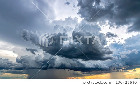 Dramatic storm clouds loom over a dark horizon as waves crash against the beach during a moody nature seascape at sunset 136429680
