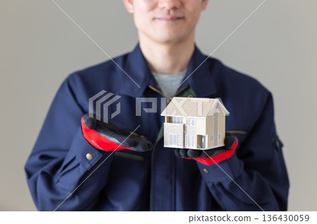 Middle-aged male businessman in work clothes holding a house model 136430059
