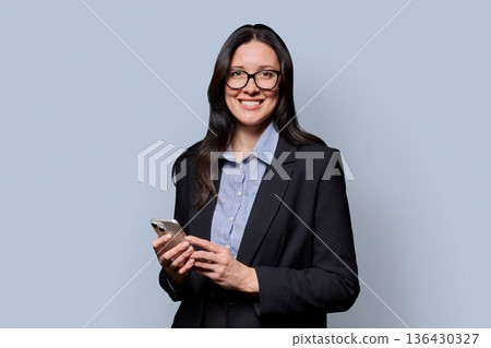 Portrait of successful middle-aged businesswoman with smartphone on grey background 136430327
