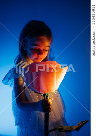 Young child interacts with oversized flower in soft blue light during creative activity 136430911