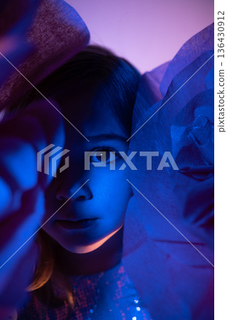 Child with blue and purple lighting peeking through paper flowers at a creative arts event indoors Child with blue and purple lighting peeking through paper flowers at a creative arts event indoors 136430912