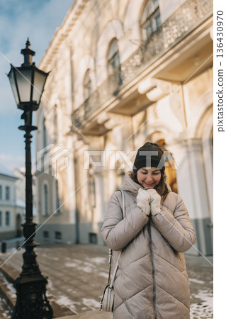 Woman stands outside a building during winter while holding her hands close to her chest 136430970
