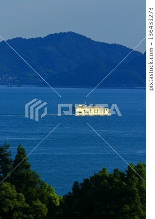 A passenger ship slowly sailing through the Seto Inland Sea bathed in the setting sun 136431273