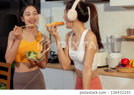 Two sporty women drinking green smoothie and eating fresh vegetables. Two sporty women drinking green smoothie and eating fresh vegetables. 136432291
