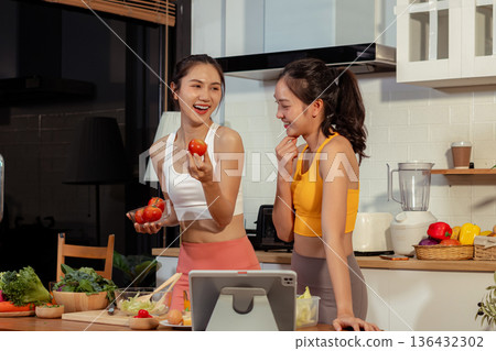 Two sporty women drinking green smoothie and eating fresh vegetables. 136432302