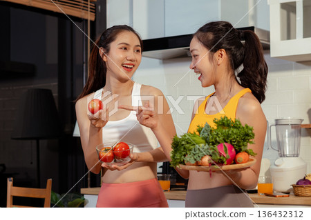 Two sporty women drinking green smoothie and eating fresh vegetables. 136432312
