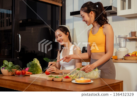 Two sporty women drinking green smoothie and eating fresh vegetables. 136432329