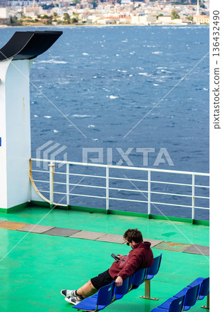 Lone passenger sitting on empty ship deck by the water 136432490