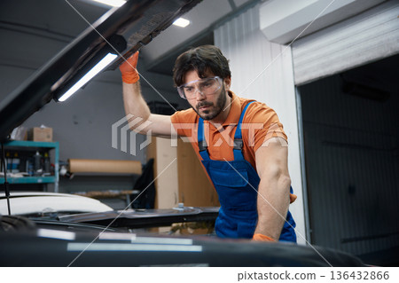 Auto mechanic inspecting car engine under the hood in garage 136432866