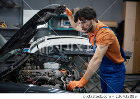 Auto mechanic inspecting car engine under the hood in garage 136432899