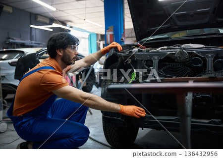 A mechanic is expertly repairing a car engine in a professional garage workshop setting A mechanic is expertly repairing a car engine in a professional garage workshop setting 136432956