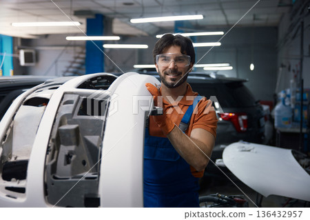Smiling automotive technician holding car bumper in garage 136432957