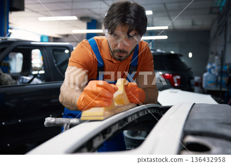 A mechanic is sanding a car bumper in an automotive garage specializing in bodywork 136432958