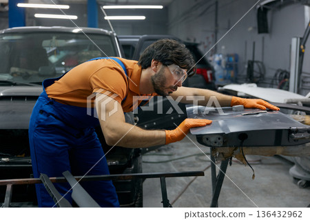 Auto technician sanding car body panel with orange gloves in workshop Auto technician sanding car body panel with orange gloves in workshop 136432962